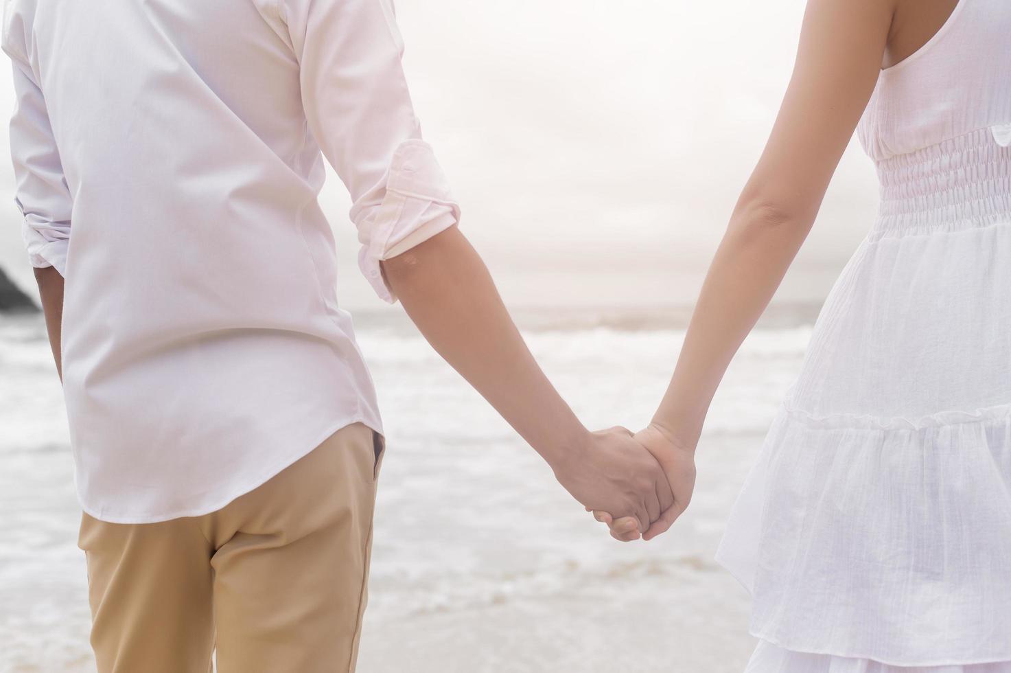 close up of a couple wearing white dress holding hands on the beach on holidays, travel, romantic, wedding concept photo