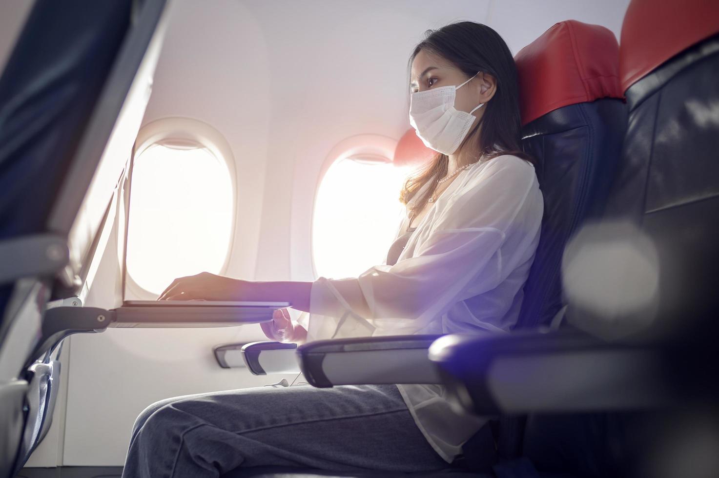 Young woman wearing face mask is using smartphone onboard, New normal travel after covid-19 pandemic concept photo