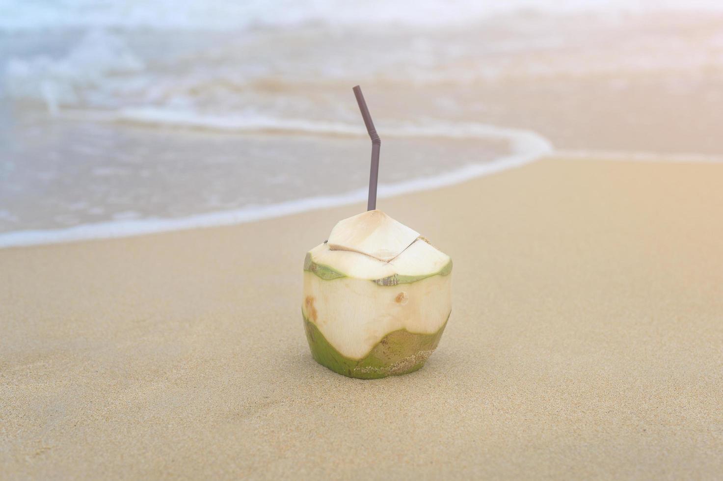 Fresh coconut with drinking straw on the beach, travel and holidays concept. photo