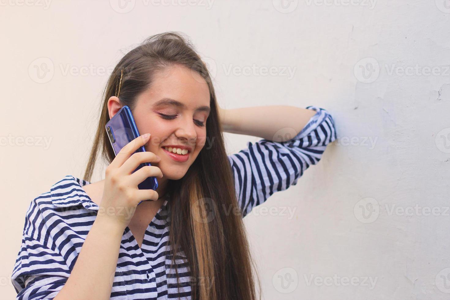 adolescente feliz hablando por teléfono cien contra la pared, una joven con el pelo largo y castaño responde la llamada foto