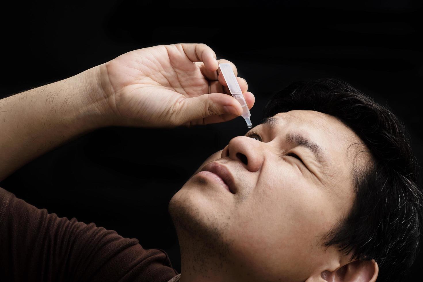 Man dropping eye drop medicine healing his eye pain with black background - health care eye medicine with people concept photo