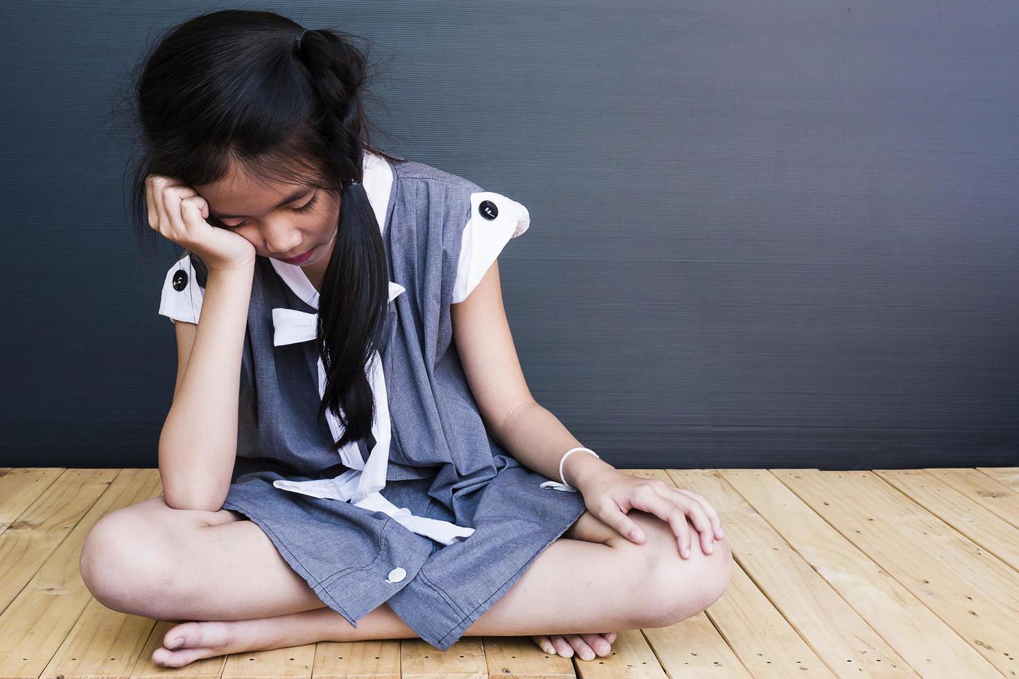 triste chica asiática sentada en el suelo de madera blanca foto