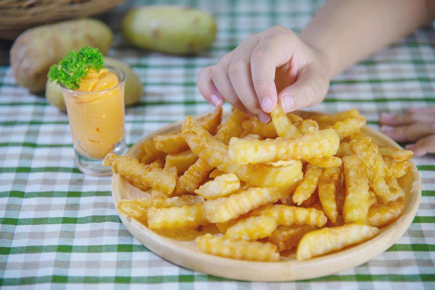 Mano sujetando una deliciosa patata frita en un plato de madera con salsa sumergida - concepto tradicional de comida rápida foto