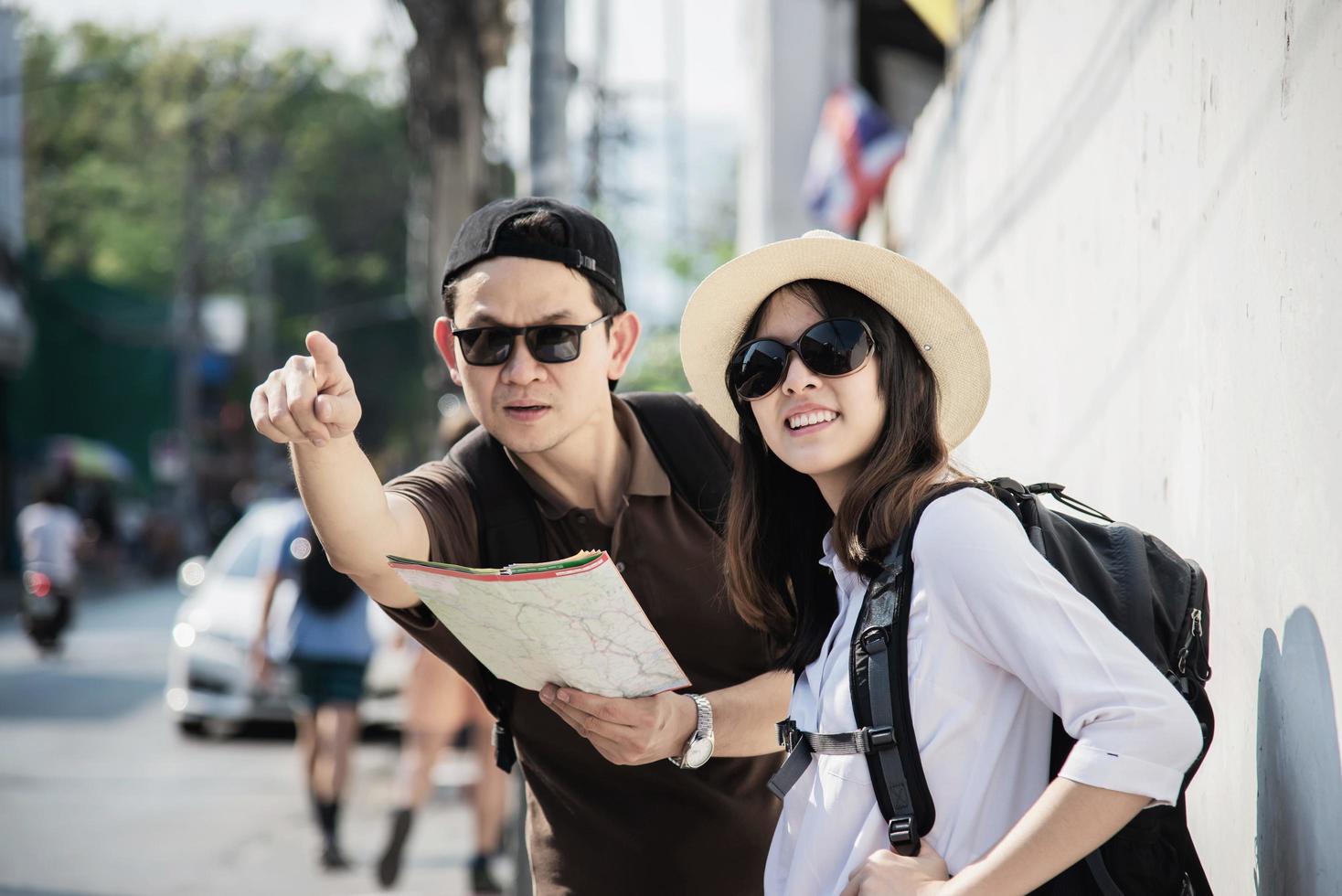 Asian backpack couple tourist holding city map crossing the road - travel people vacation lifestyle concept photo