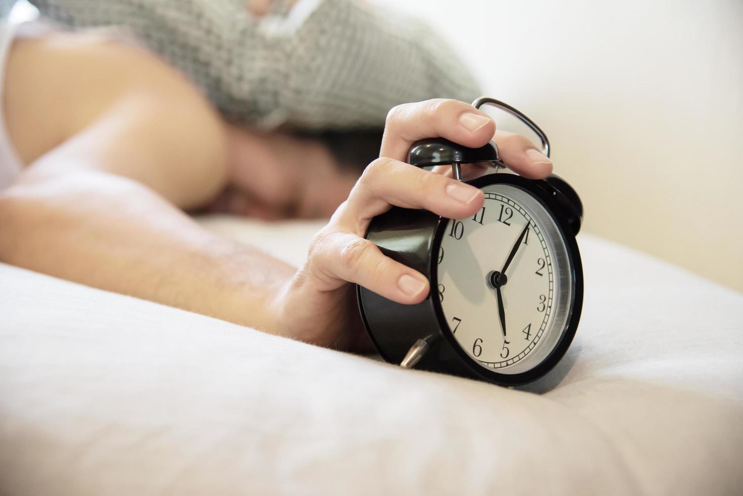 hombre soñoliento sosteniendo el despertador por la mañana con despertar tardío - concepto de vida diaria en casa foto