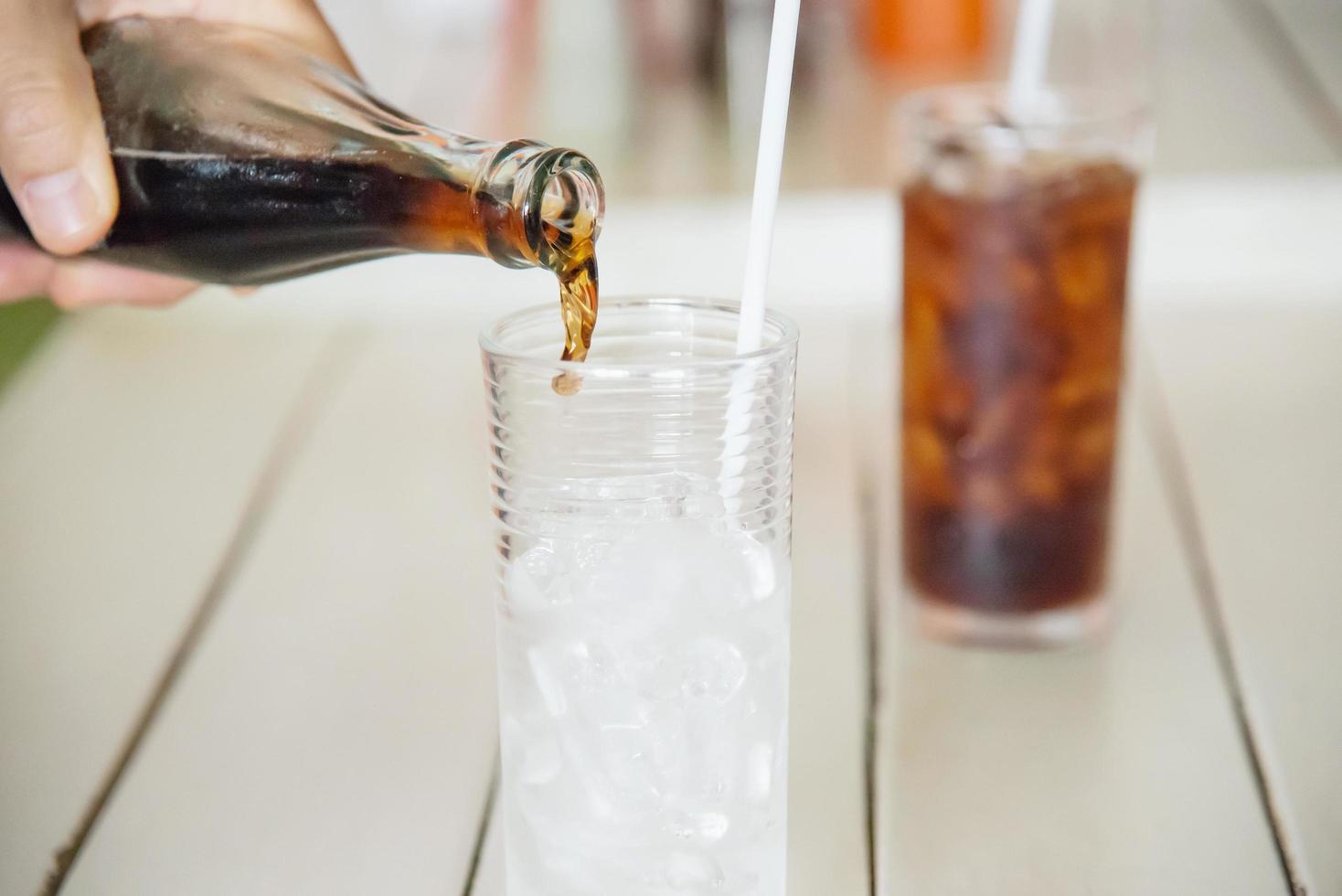 vierta a mano un refresco en un vaso con hielo - concepto de bebida fría para refrescos sedientos foto