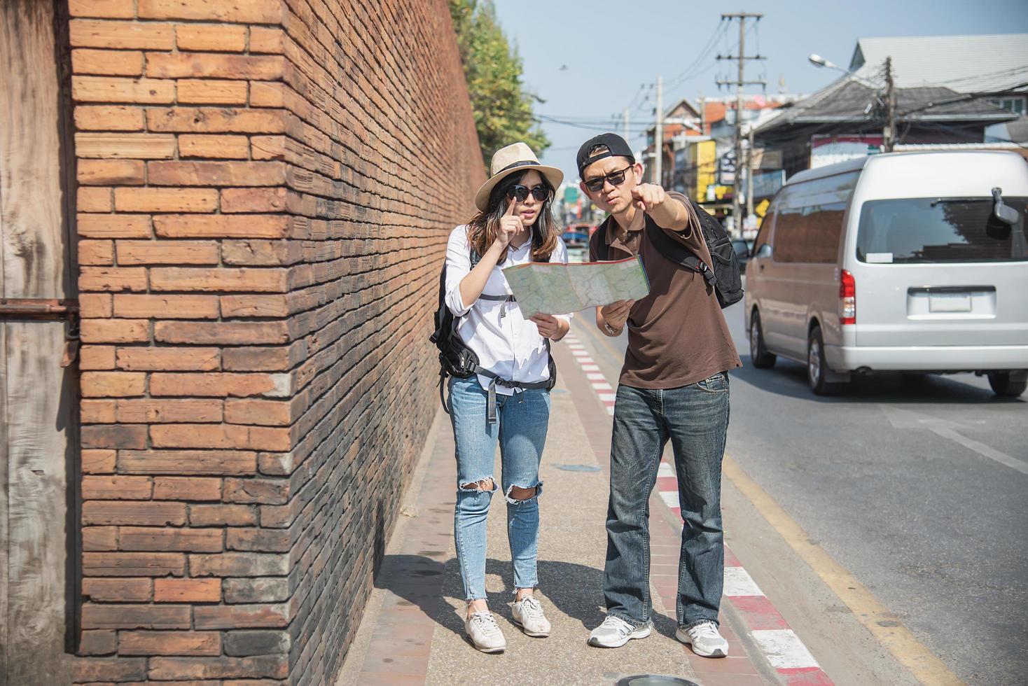 Asian backpack couple tourist holding city map crossing the road - travel people vacation lifestyle concept photo