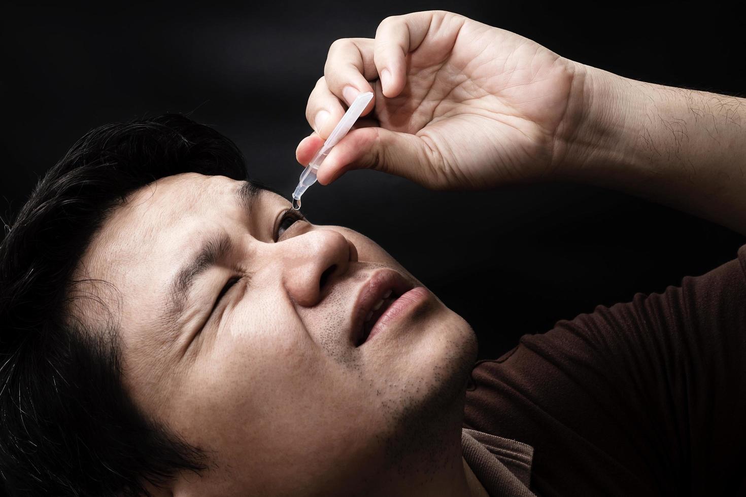 Man dropping eye drop medicine healing his eye pain with black background - health care eye medicine with people concept photo