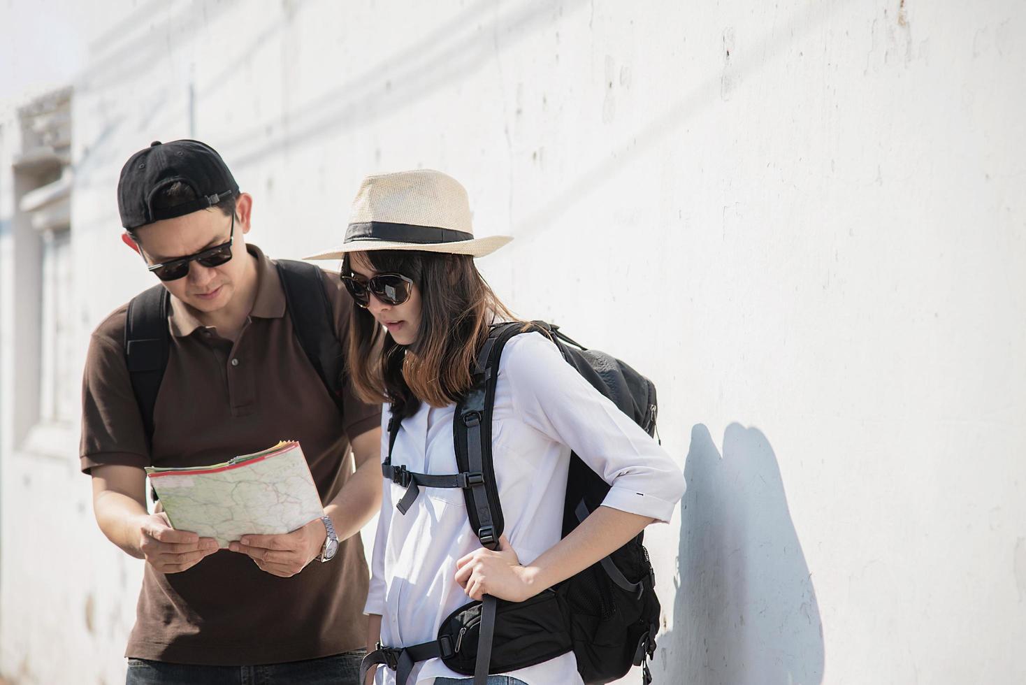 Asian backpack couple tourist holding city map crossing the road - travel people vacation lifestyle concept photo