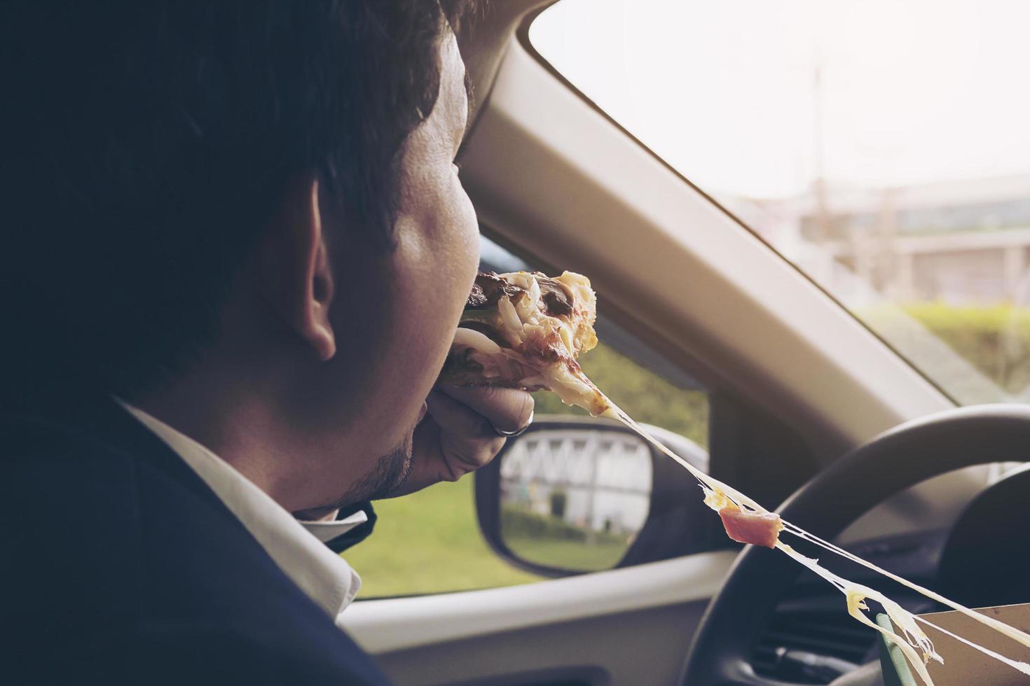 Business man eating pizza while driving a car dangerously photo