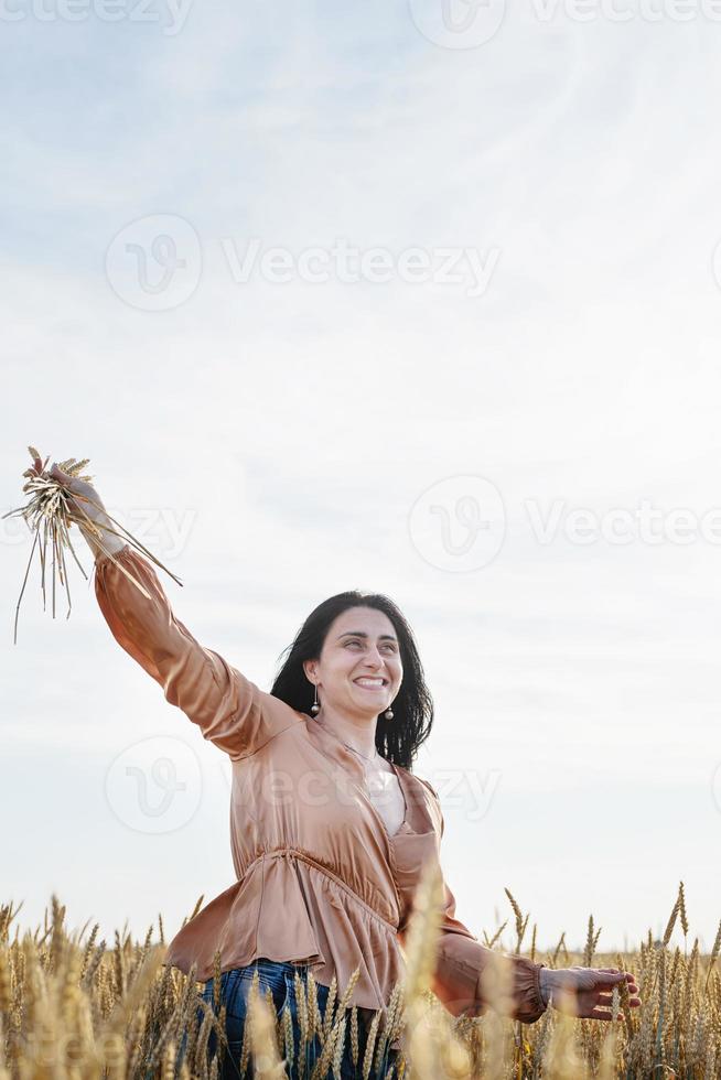 mujer adulta media con camisa beige parada en un campo de trigo con amanecer en el fondo, vista trasera foto