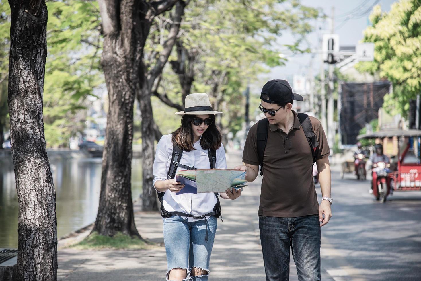 Asian backpack couple tourist holding city map crossing the road - travel people vacation lifestyle concept photo