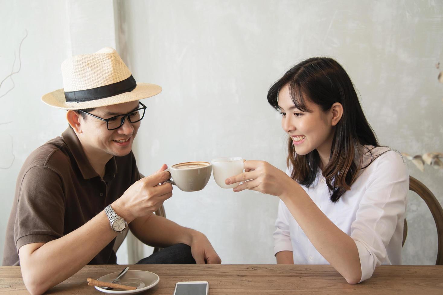 hombre y mujer casuales hablando alegremente mientras toman café y miran el teléfono móvil - estilo de vida feliz en la cafetería foto