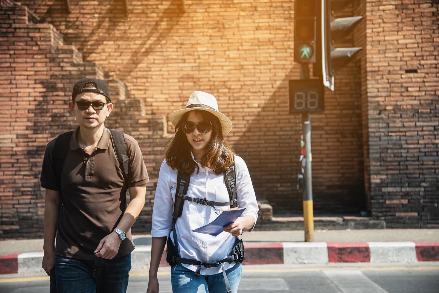 mochila asiática pareja turista sosteniendo un mapa de la ciudad cruzando la carretera - gente de viaje concepto de estilo de vida de vacaciones foto