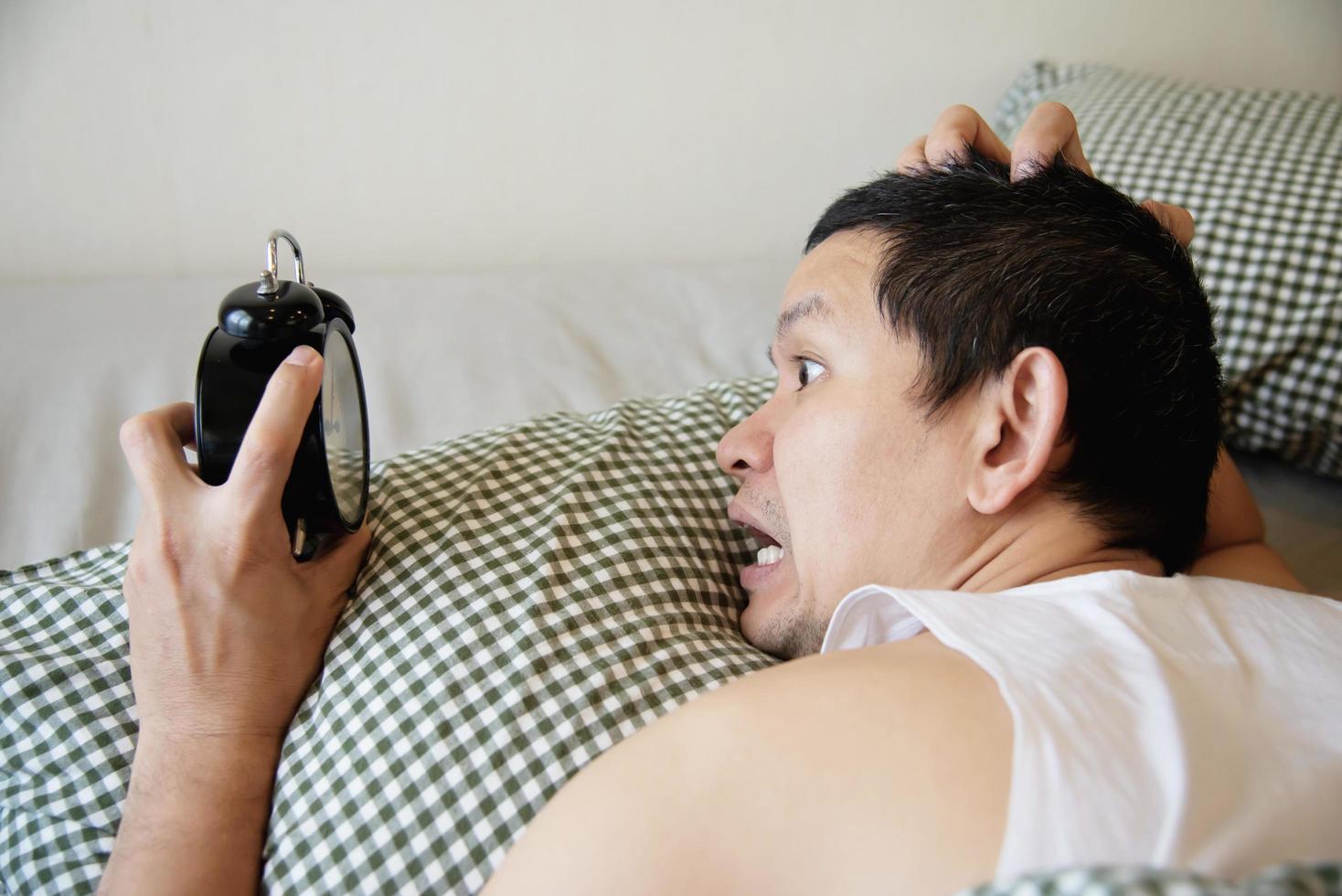 hombre soñoliento sosteniendo el despertador por la mañana con despertar tardío - concepto de vida diaria en casa foto