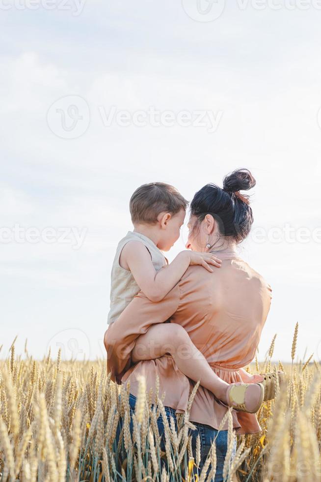 familia feliz de madre y niño pequeño caminando en el campo de trigo, abrazándose y besándose foto