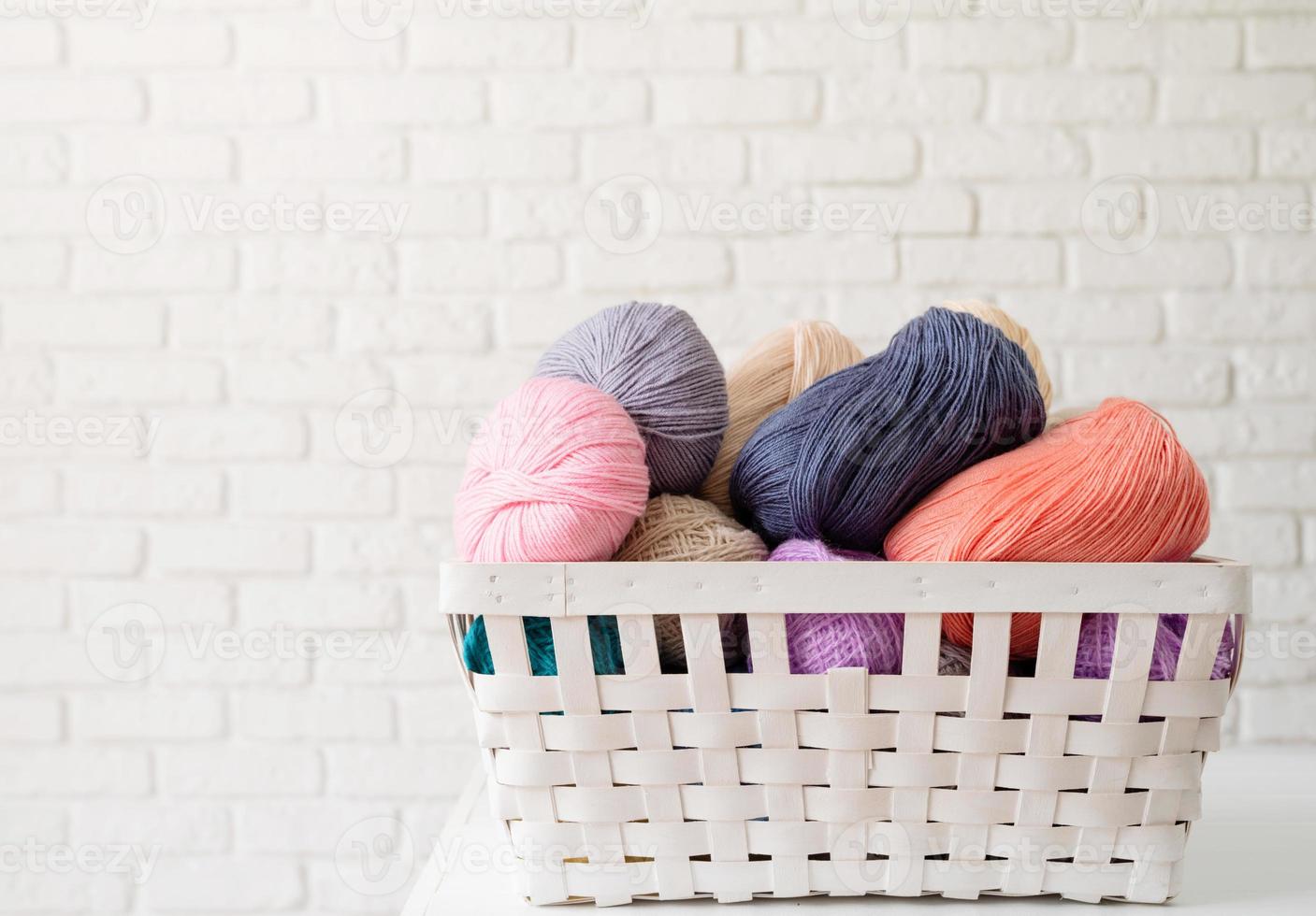 pastel colored yarn wool in a white basket on white brick wall background photo