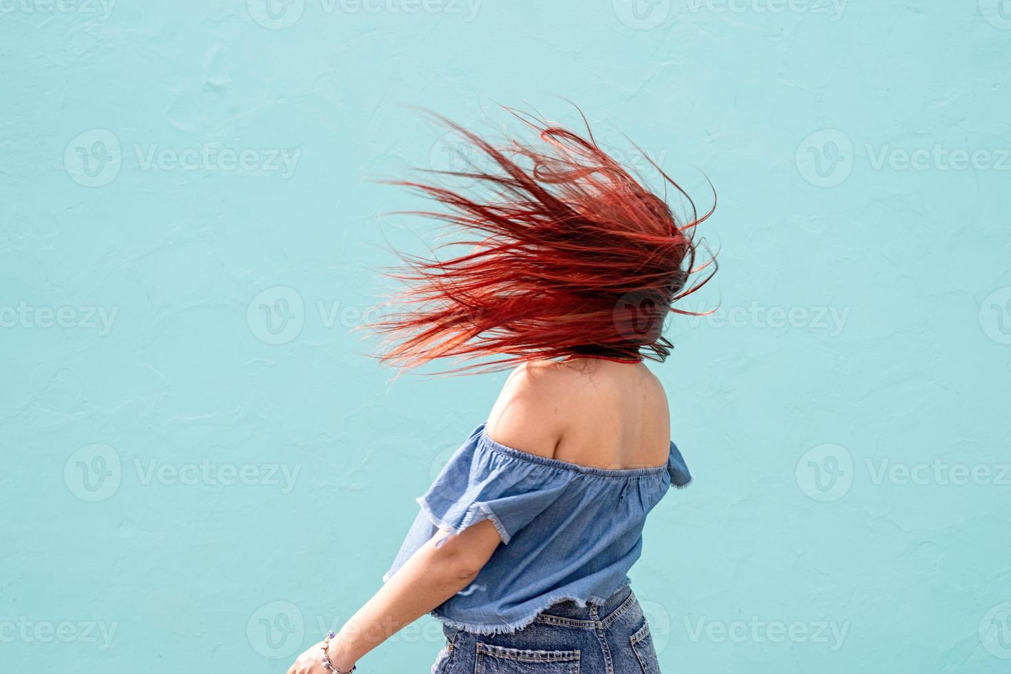 alegre mujer de moda con el pelo rojo bailando sobre fondo de pared azul en la calle foto