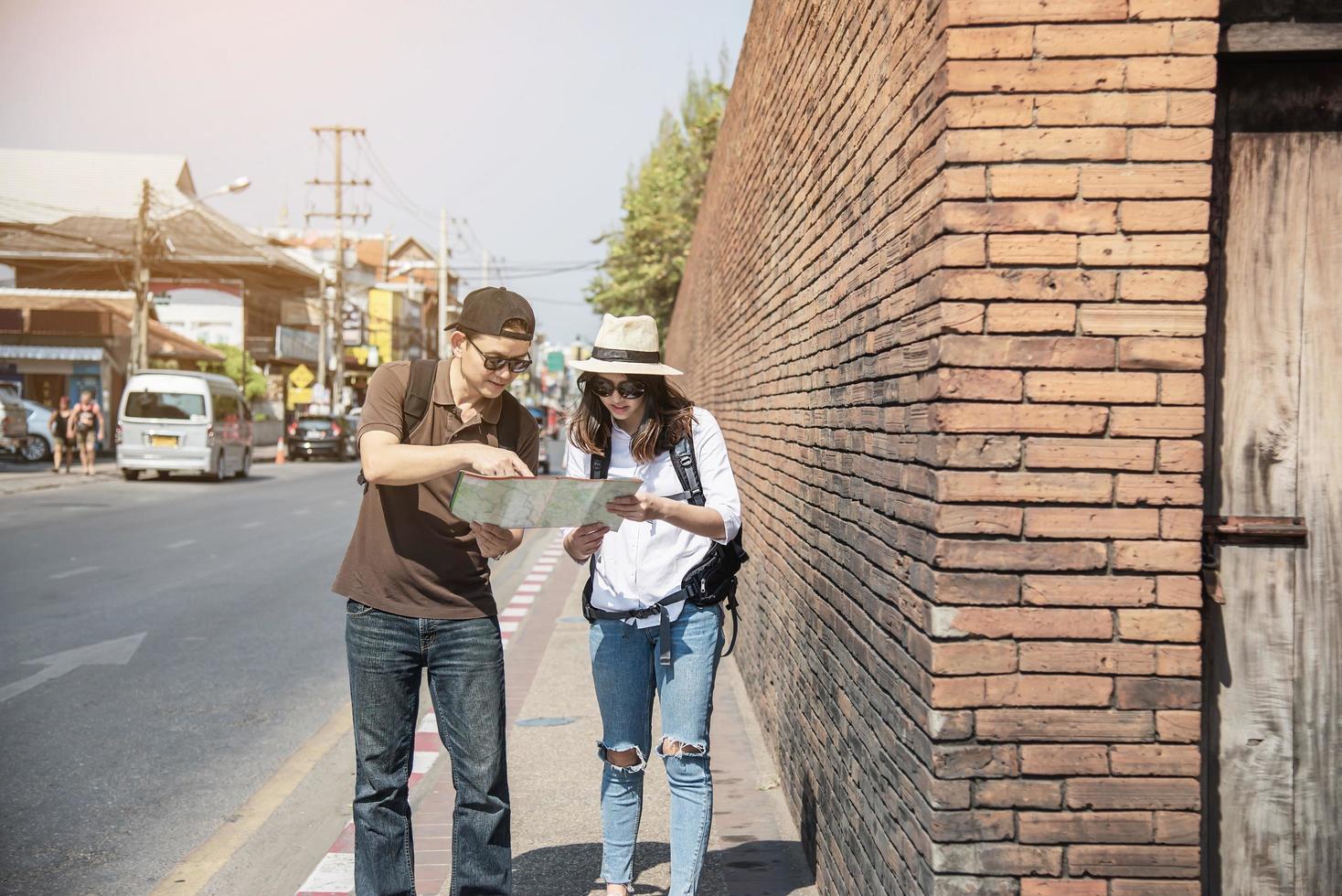 Asian backpack couple tourist holding city map crossing the road - travel people vacation lifestyle concept photo