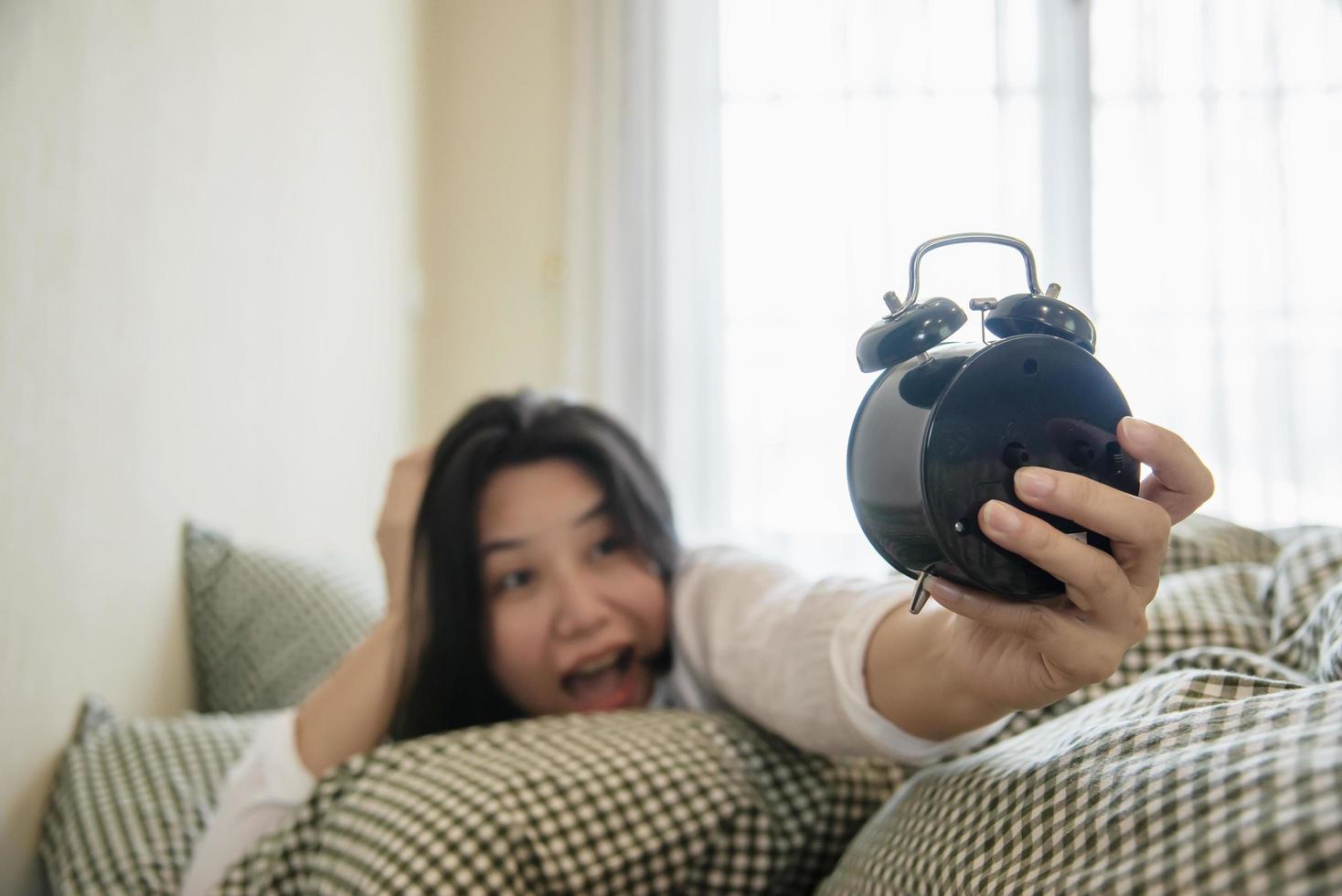 Sleepy woman reaching  holding the alarm clock in the morning with late wake up - every day life at home concept photo