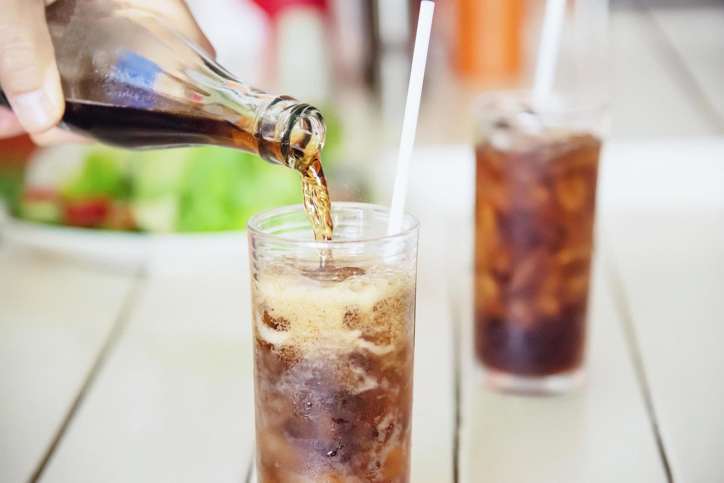 vierta a mano un refresco en un vaso con hielo - concepto de bebida fría para refrescos sedientos foto