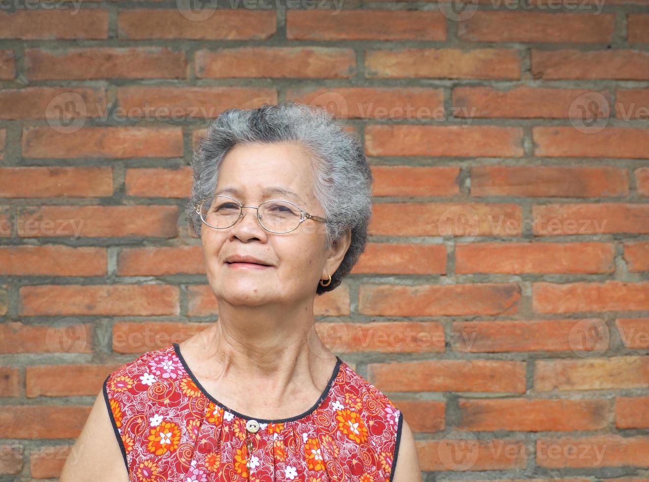 una anciana asiática de pie y mirando a la cámara con fondo de pared de ladrillo foto