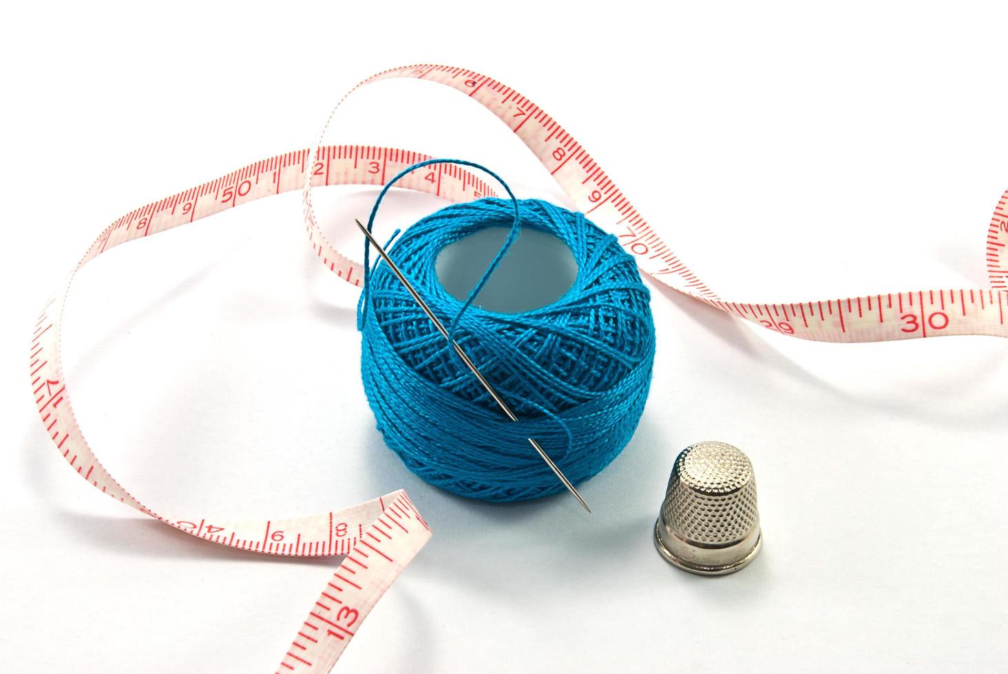 Thimble,needles and blue thread ball  for sewing on a background thread photo