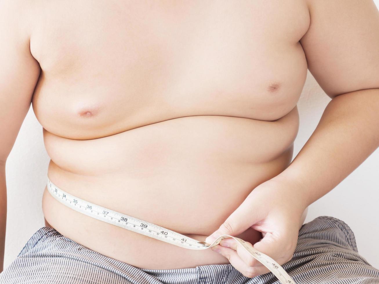 A fat boy is measuring his belly using tape meter photo