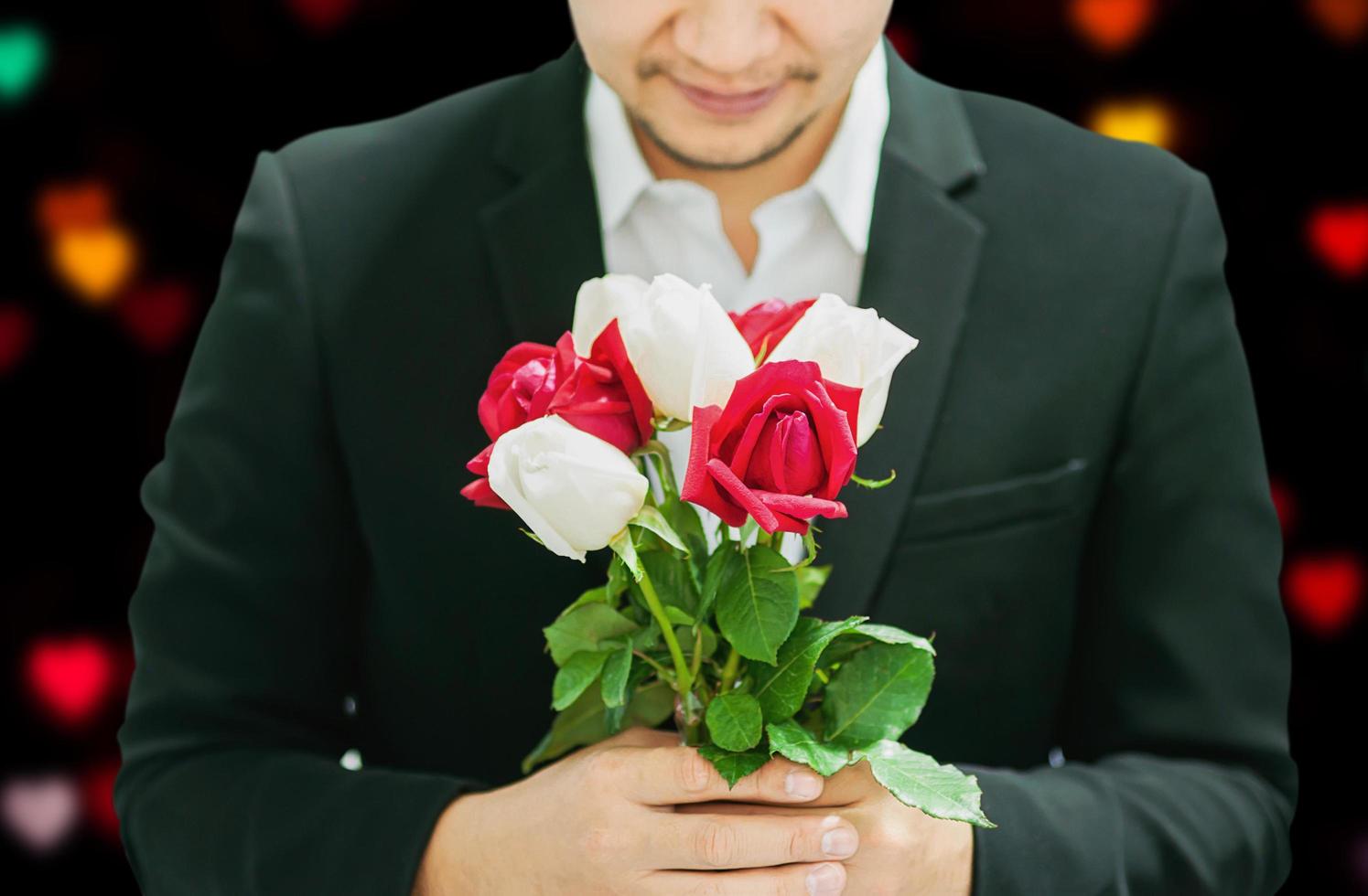Man giving red and white bouquet roses to somebody in valentine day or other love festival event with black and blur colorful heart bokeh background photo