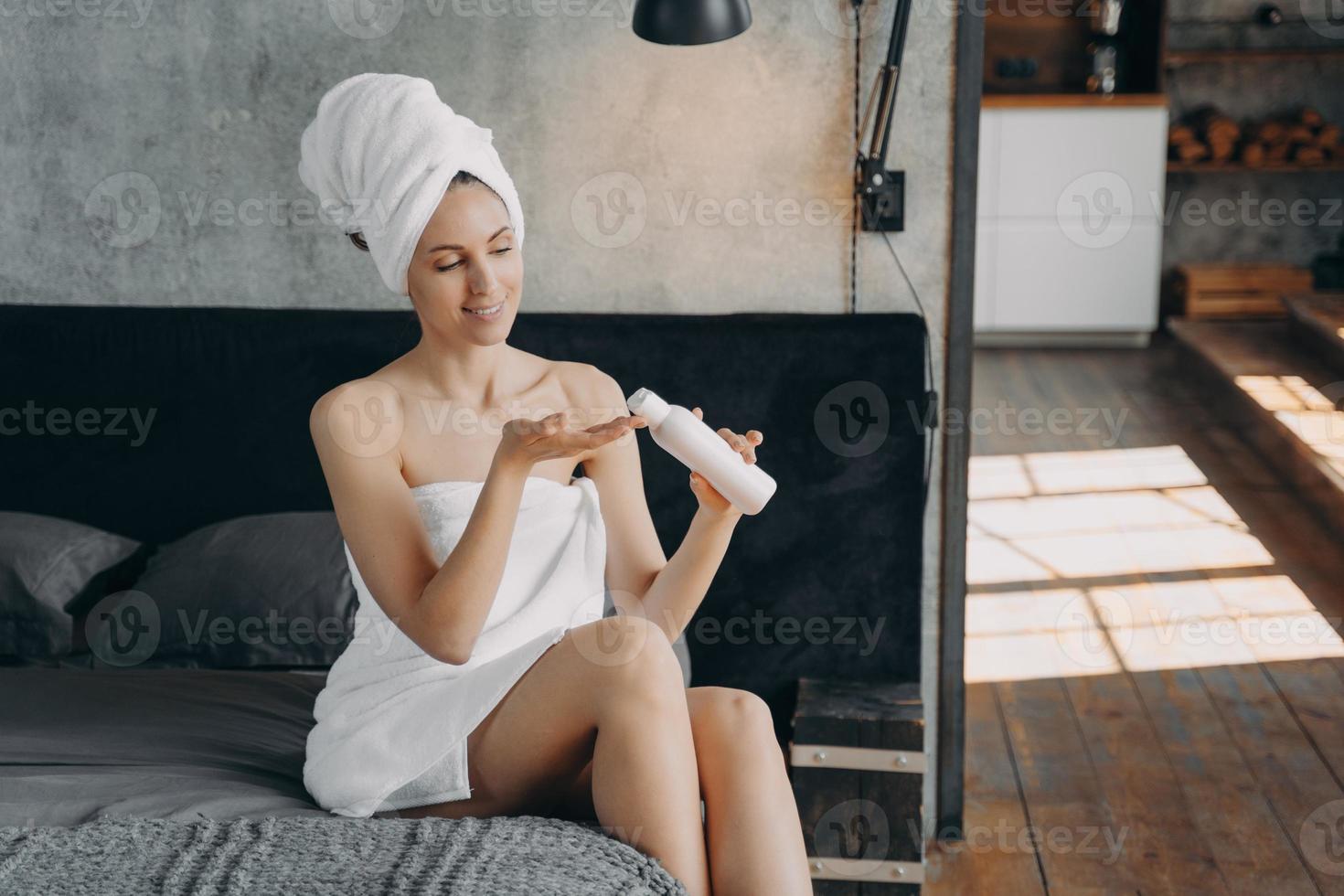 Happy girl applying body moisturizing lotion squeezing it out from bottle after bathing at home. photo
