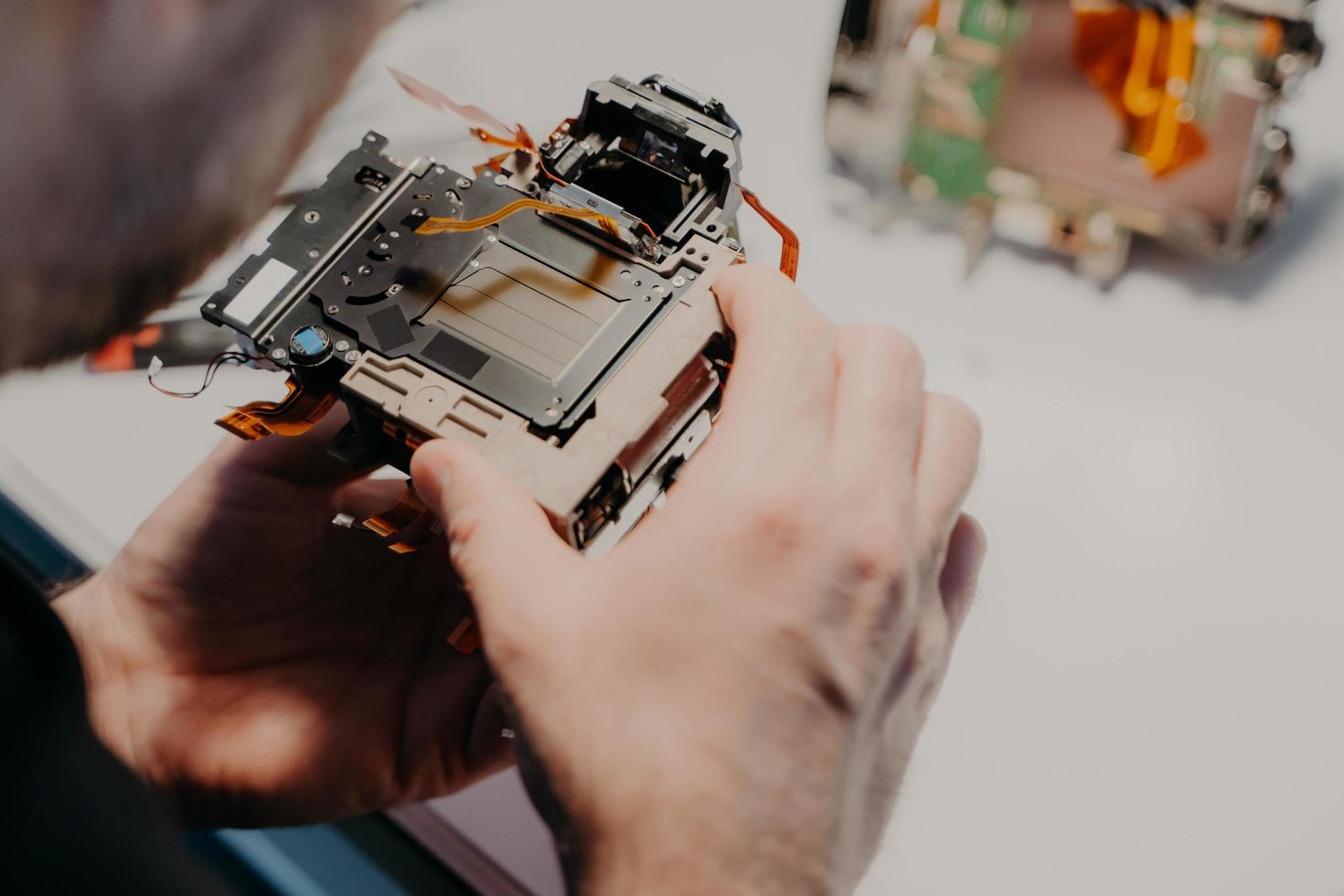 Engineers hands holds broken photo camera, poses against workspace, repairs digital device or professional dslr camera. Professional specialist with disassembled equipment