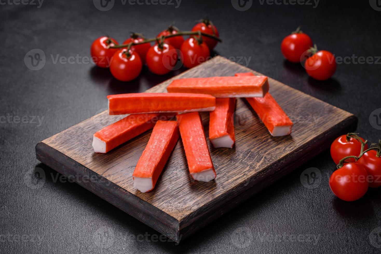 Crab sticks on a cutting Board with a knife. On black concrete background photo