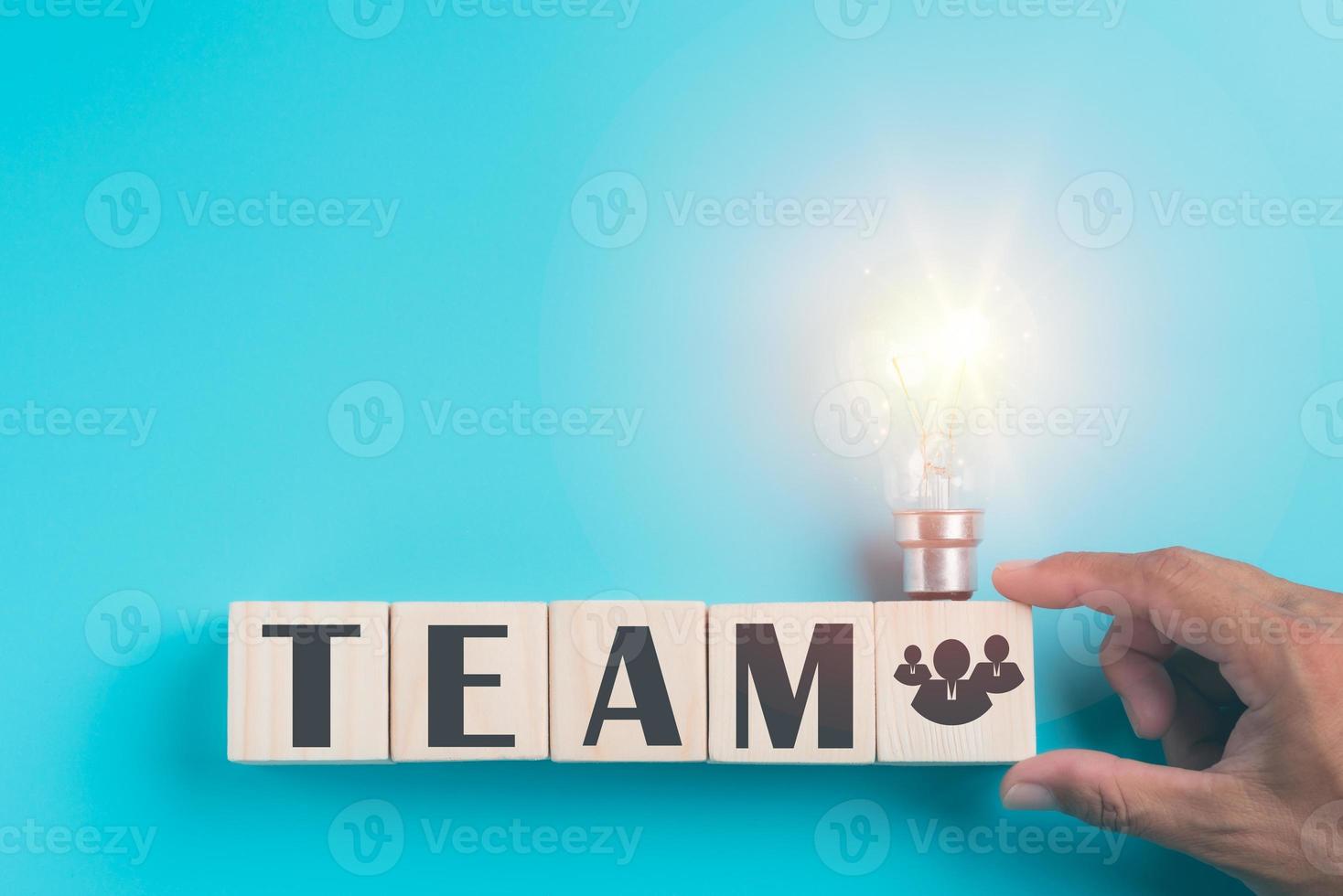 Hand holding a wooden block, a light bulb, all on a blue background, photo