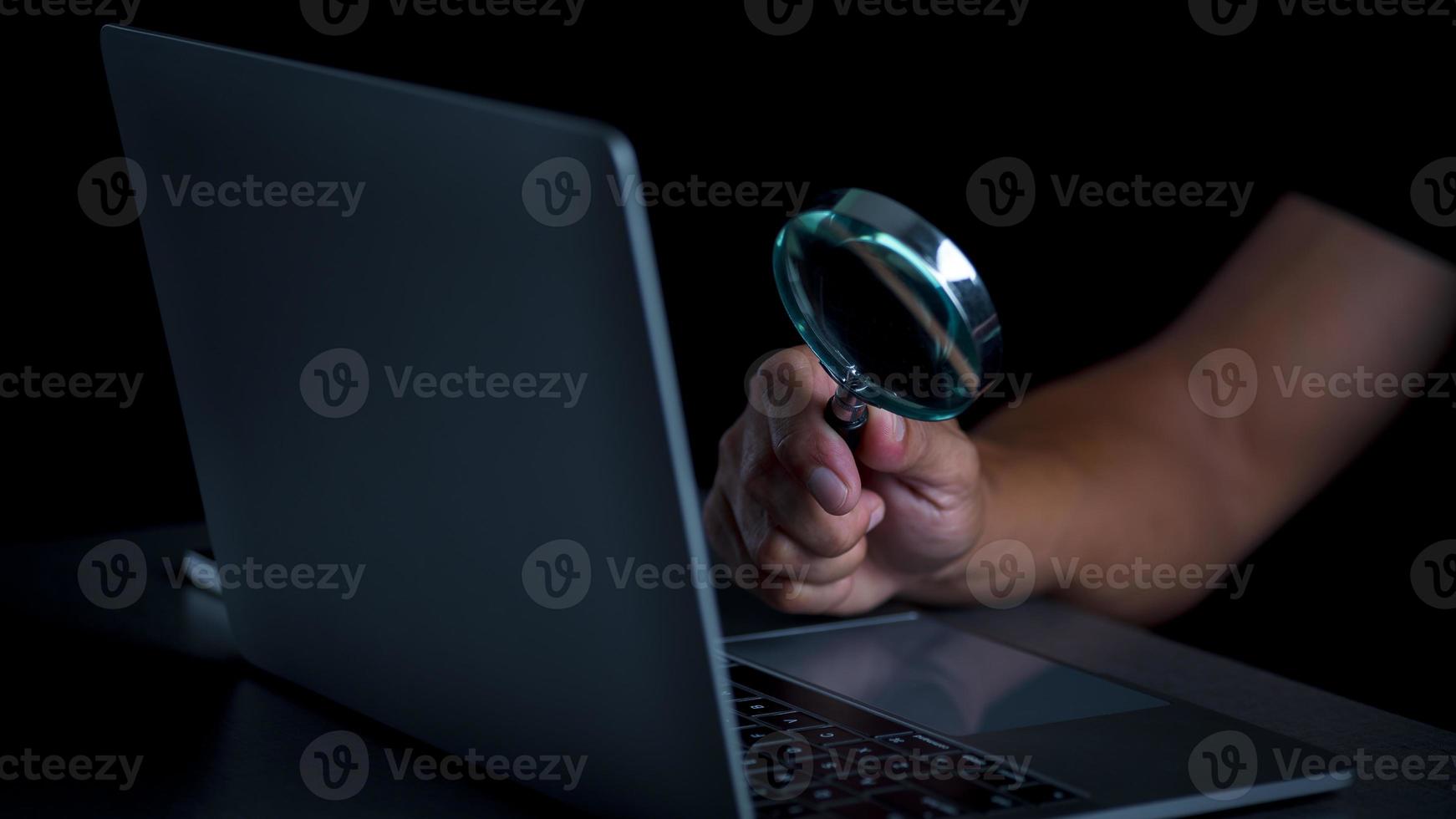 A magnifying glass in a man's hand and he is looking at a notebook computer, the concept of searching for information in the internet world search technology Search Engine Optimization. photo