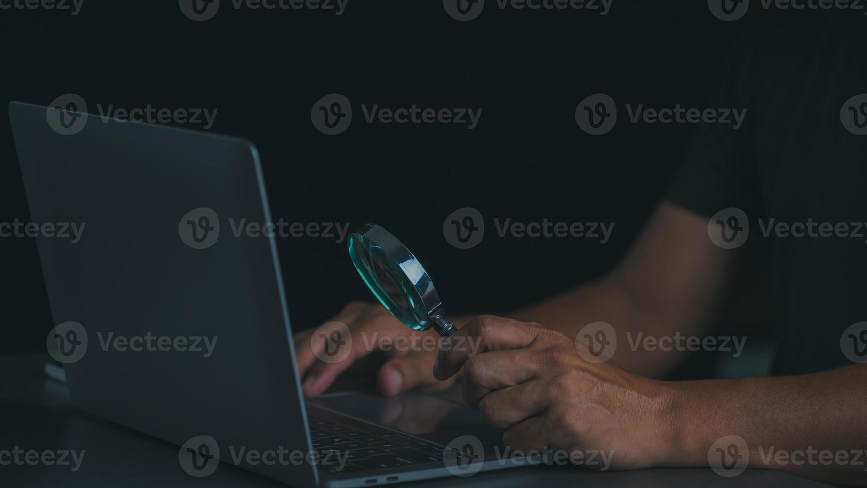 A magnifying glass in a man's hand and he is looking at a notebook computer. photo