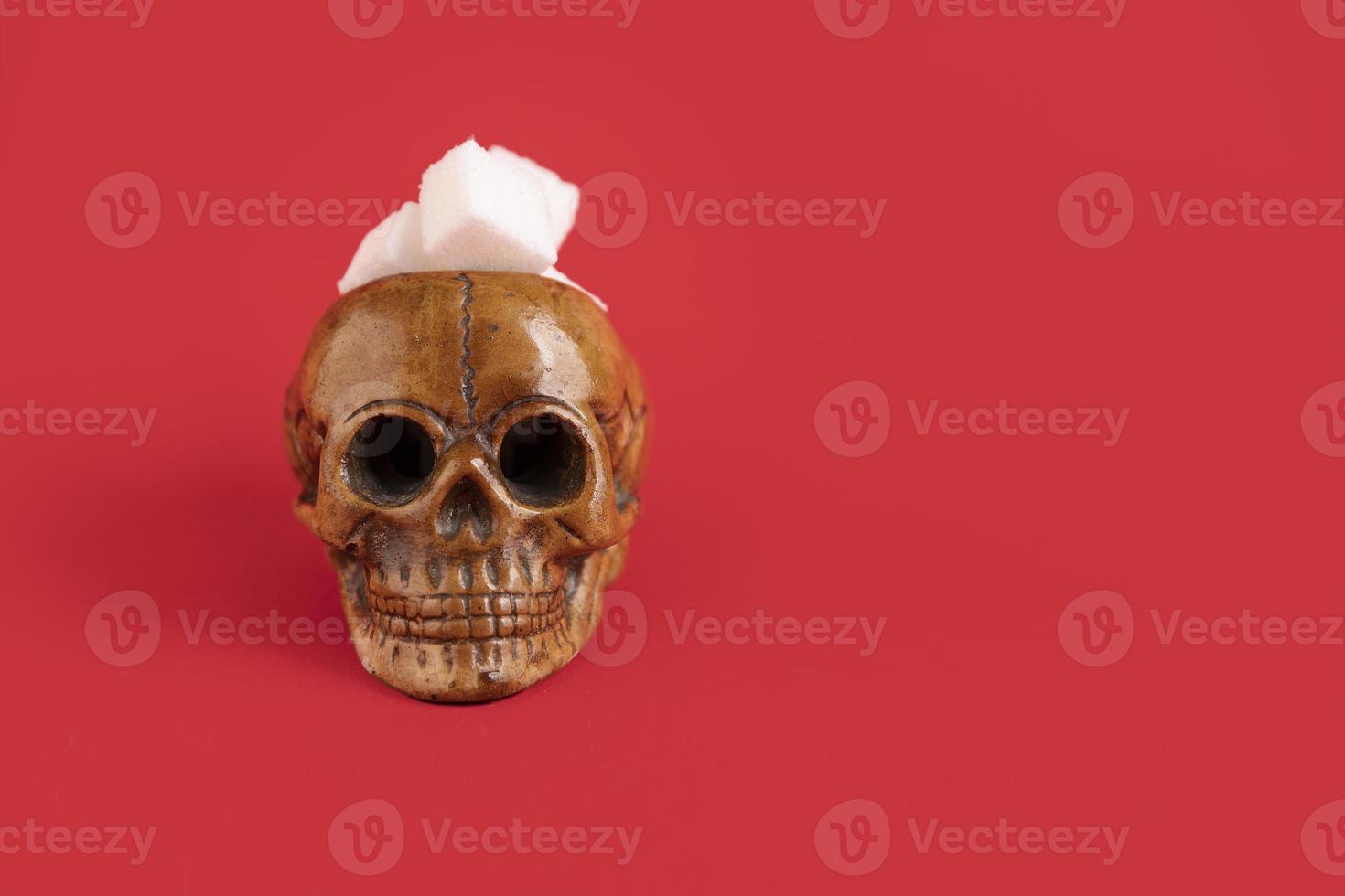 Human skull filled with refined white sugar cubes on a red background. Selective focus. Copy space. photo