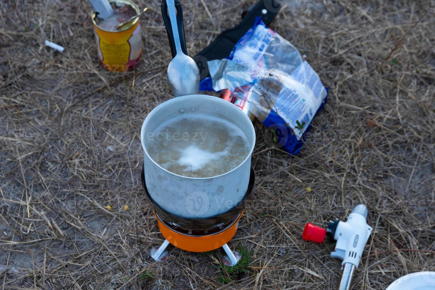 Pasta in a spoon and boiling water in a saucepan, tourist food in nature. photo