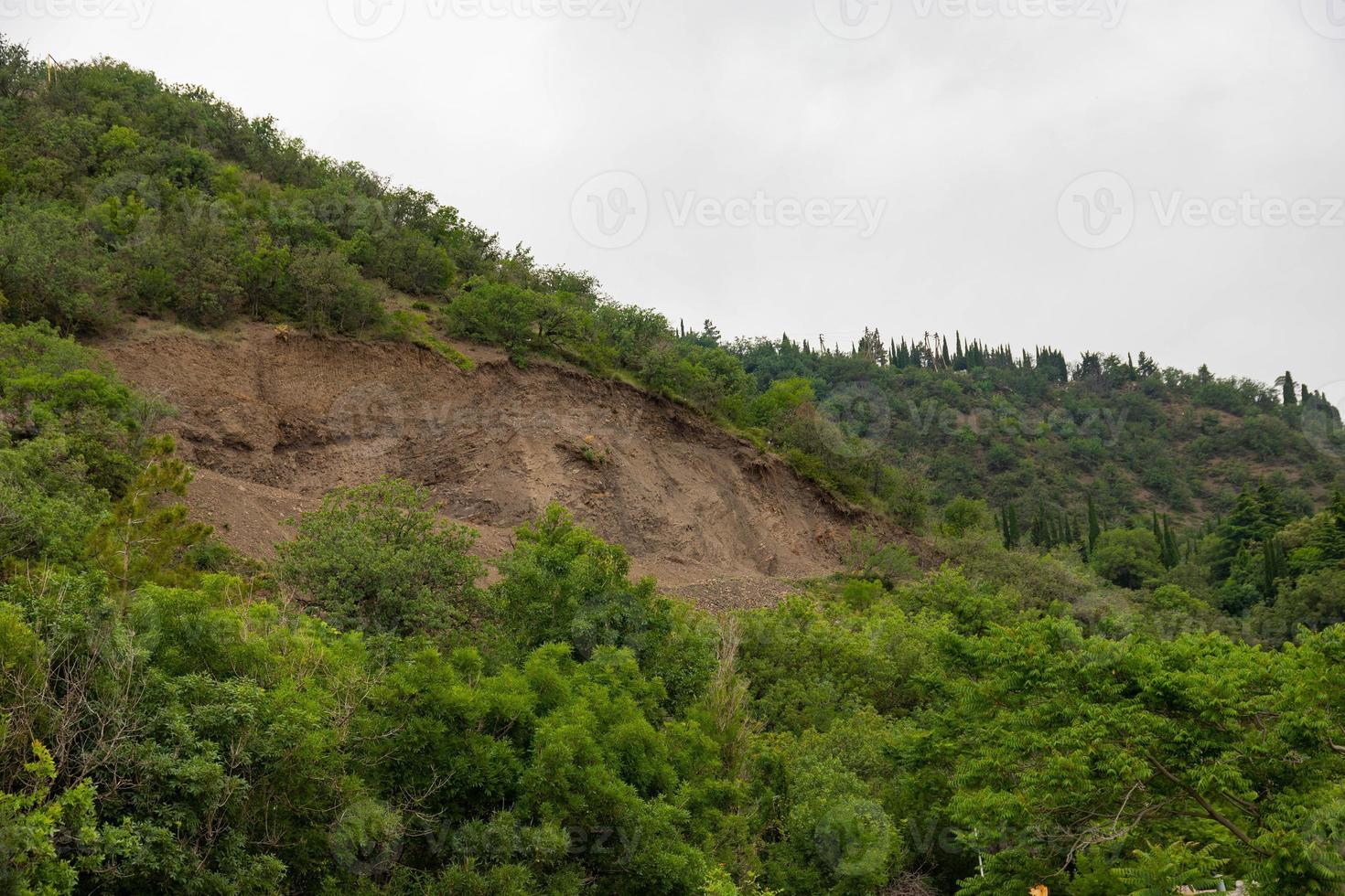 A mountain landslide in an ecologically dangerous zone, the fall of large layers of earth blocking the road. Soil under erosion conditions. photo