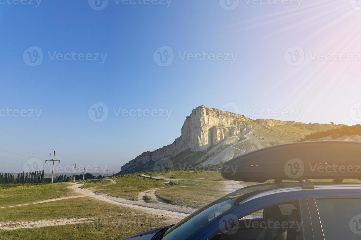 car for travel with a roof rack on a mountain road, against the backdrop of the White Rock. photo