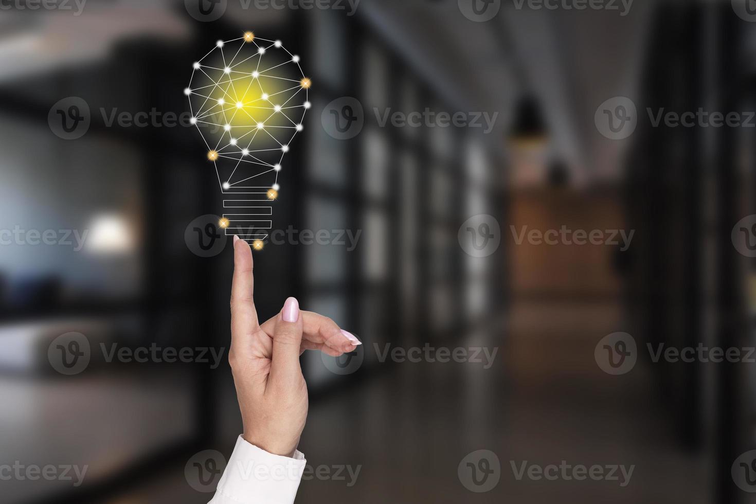 A woman's hand points to a glowing light bulb on the background of the office. Concept of innovation, ideas in business. photo