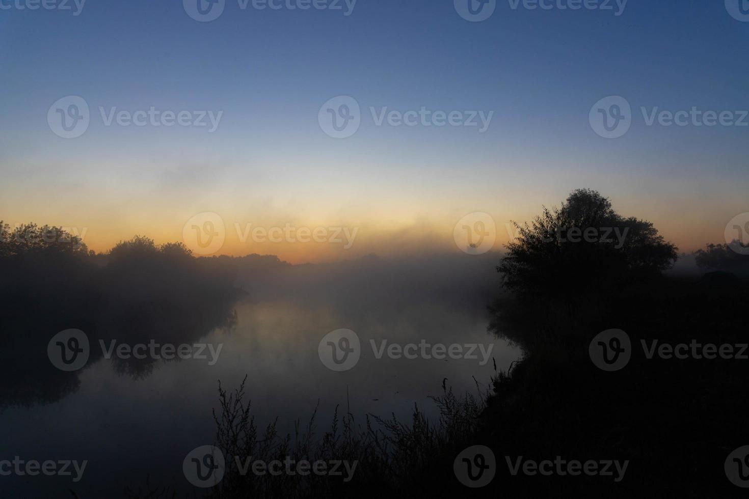 Foggy morning on a European river with fresh green grass in the sun. The rays of the sun through the tree. photo