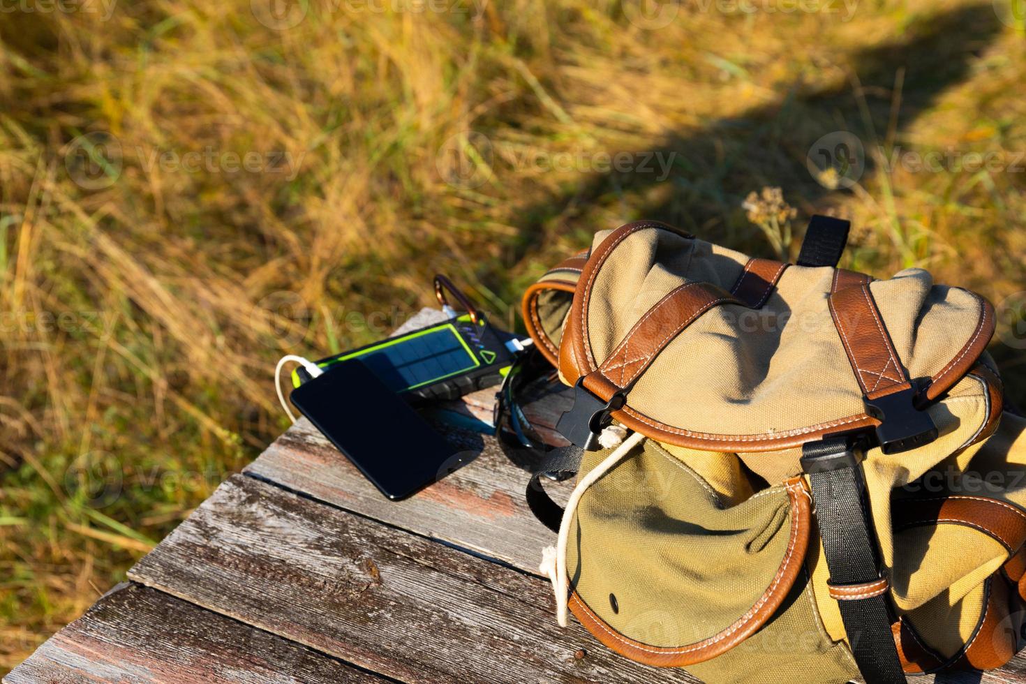 Solar energy battery device, power bank and telephone on a wooden table with a backpack. Solar charge your smartphone. Selective focus photo
