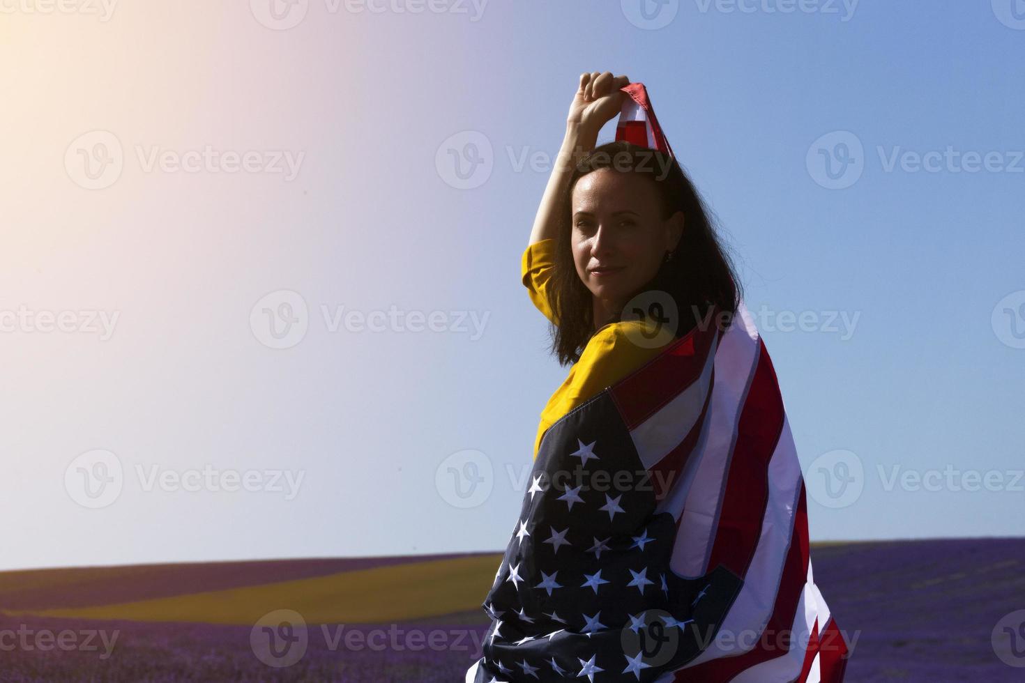 una mujer joven de cabello oscuro que sostiene la bandera de los estados unidos de américa contra el cielo soleado. día conmemorativo y concepto del día de la independencia de estados unidos. foto