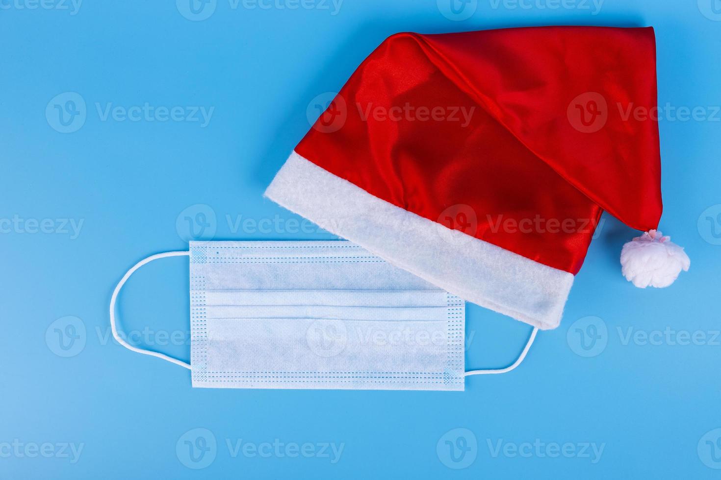 santa claus hat and medical disposable safety mask on blue paper background photo