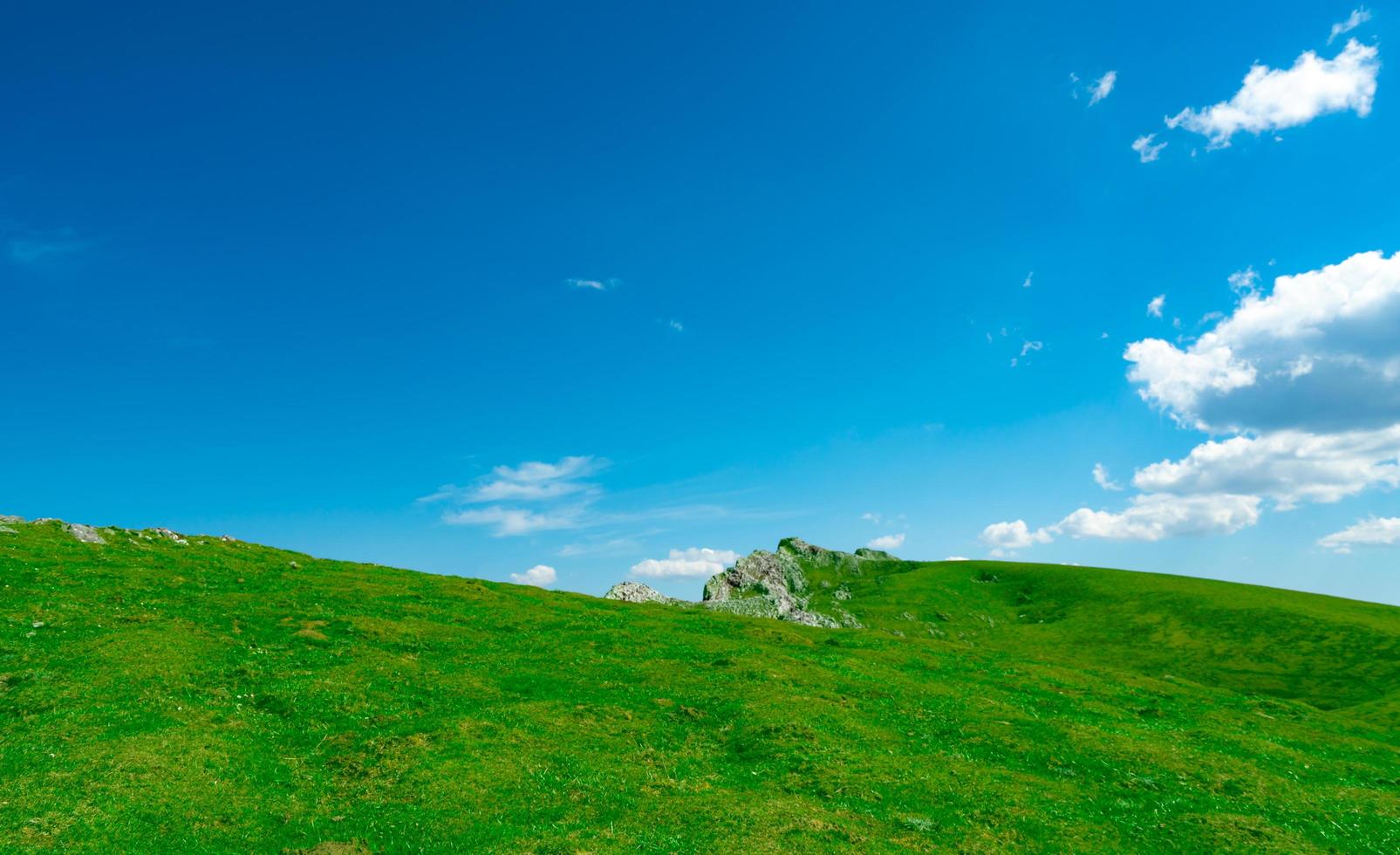 Landscape of green grass and rock hill in spring with beautiful blue sky and white clouds. Countryside or rural view. Nature background in sunny day. Fresh air environment. Stone on the mountain. photo