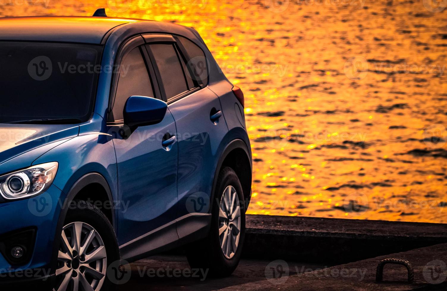 Blue compact SUV car with sport and modern design parked on concrete road by sea at sunset. Environmentally friendly technology. Hybrid and electric car technology. Car parking space. summer travel. photo
