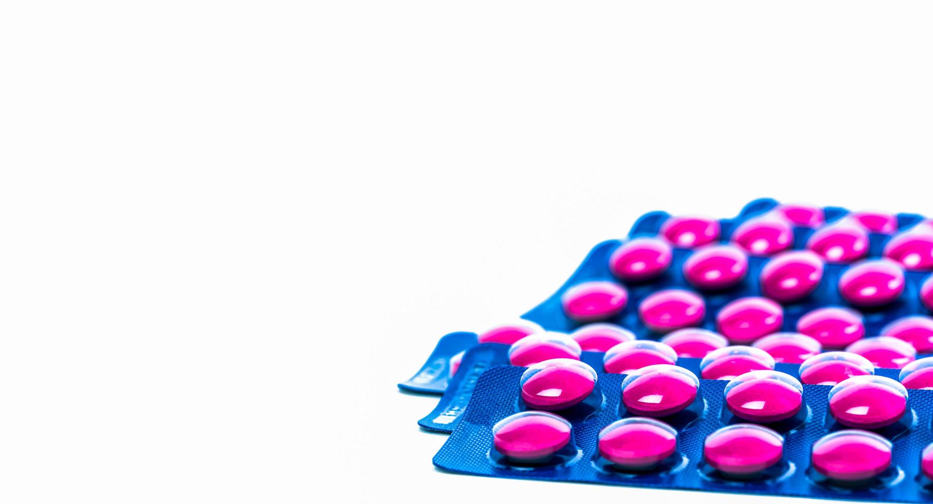 Pink tablets pill in blue blister pack isolated on white background. Painkiller medicine. Pharmaceutical industry. Medicine for treat migraine headache, fever, toothache. Pharmacy drugstore products. photo