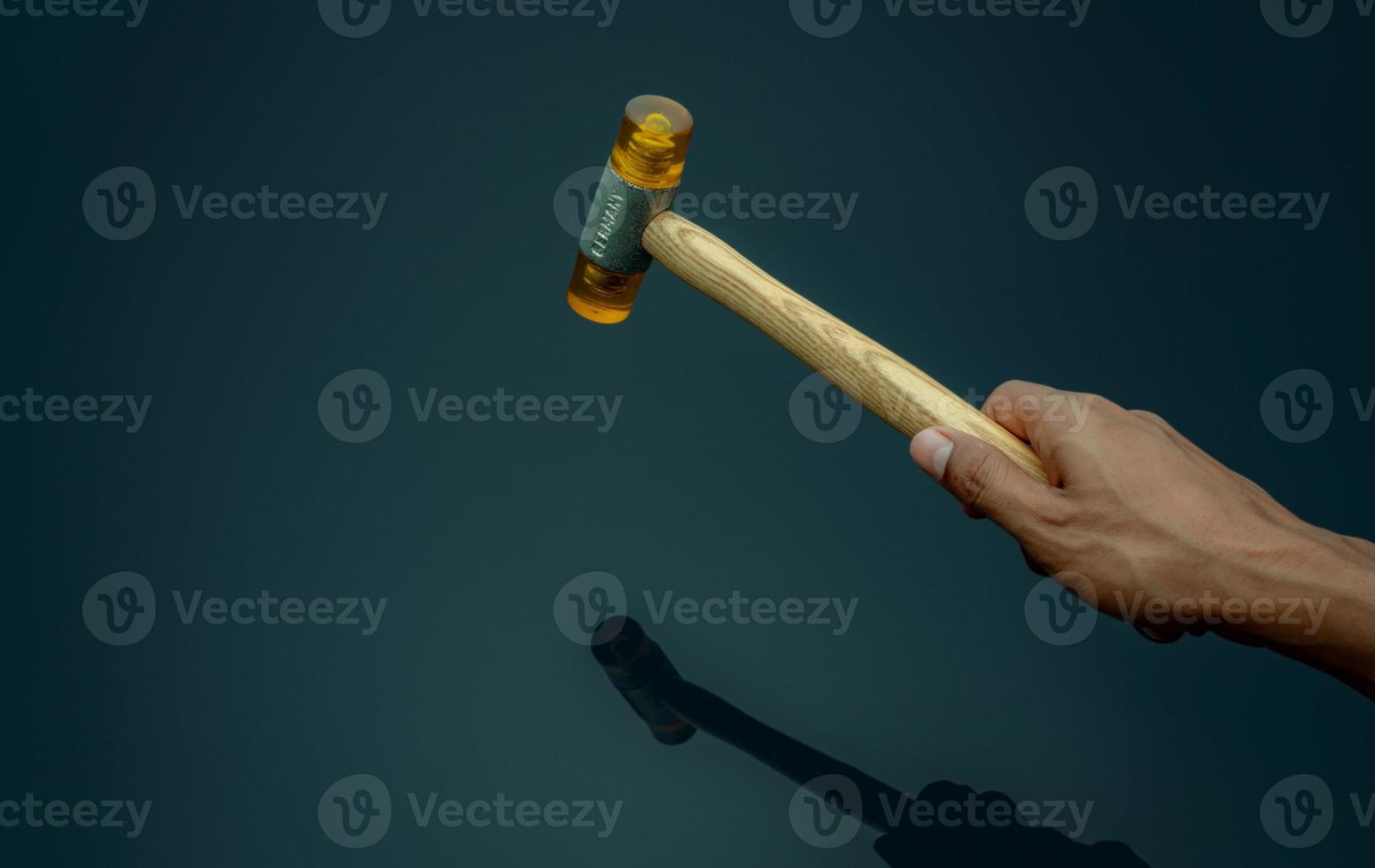 Man's hand holding plastic hammer isolated on dark background. Male worker's hand hold wood handle of plastic hammer. Hammer head made of soft and tough yellow plastic that not damage workpiece. photo