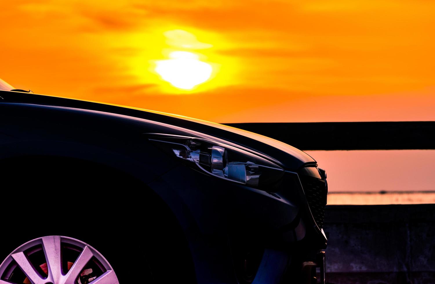 Blue compact SUV car with sport and luxury design parked on concrete road by the sea at sunset. Electric car technology and business. Hybrid auto and automotive industry. Tropical road trip travel. photo