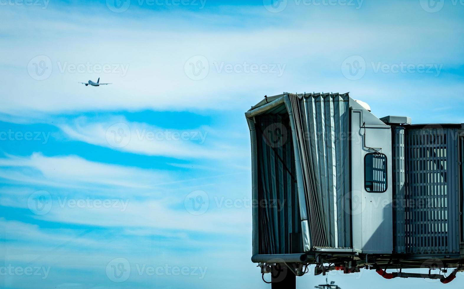 Jet bridge after commercial airline take off at the airport and the plane flying in the blue sky and white clouds. Aircraft passenger boarding bridge docked. Departure flight of international airline. photo